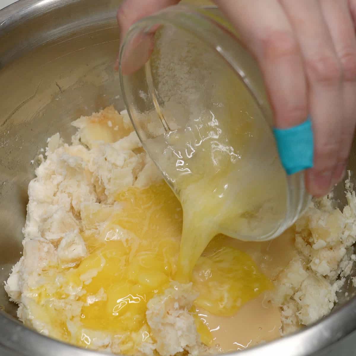 Adding melted butter to mashed cassava in a bowl.