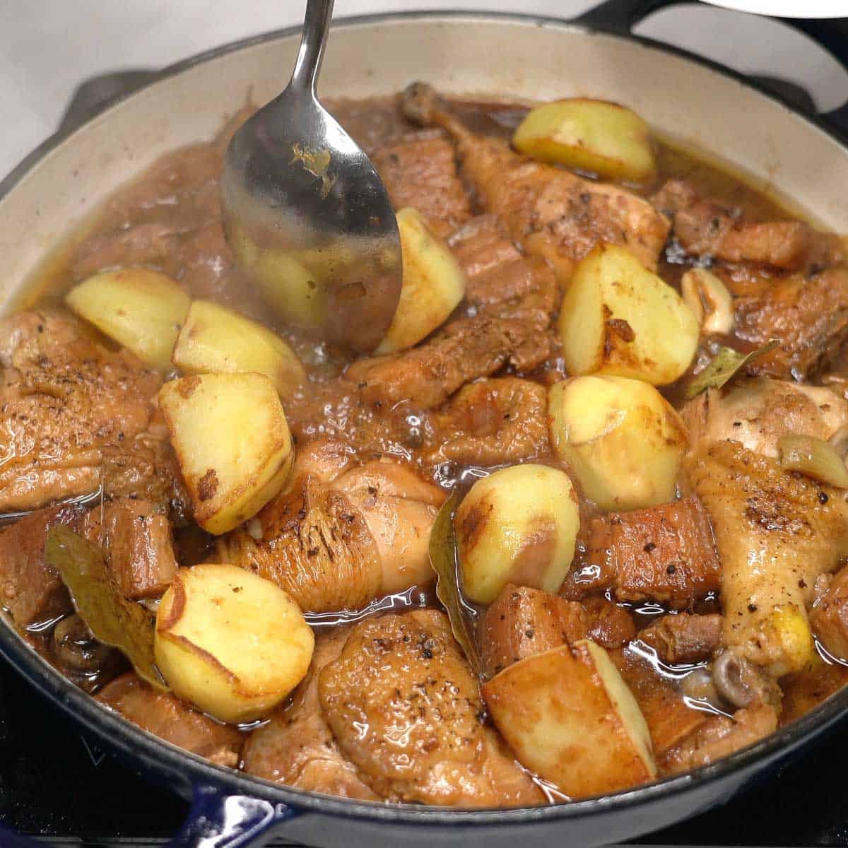Adding browned potatoes to the adobo in the pan.
