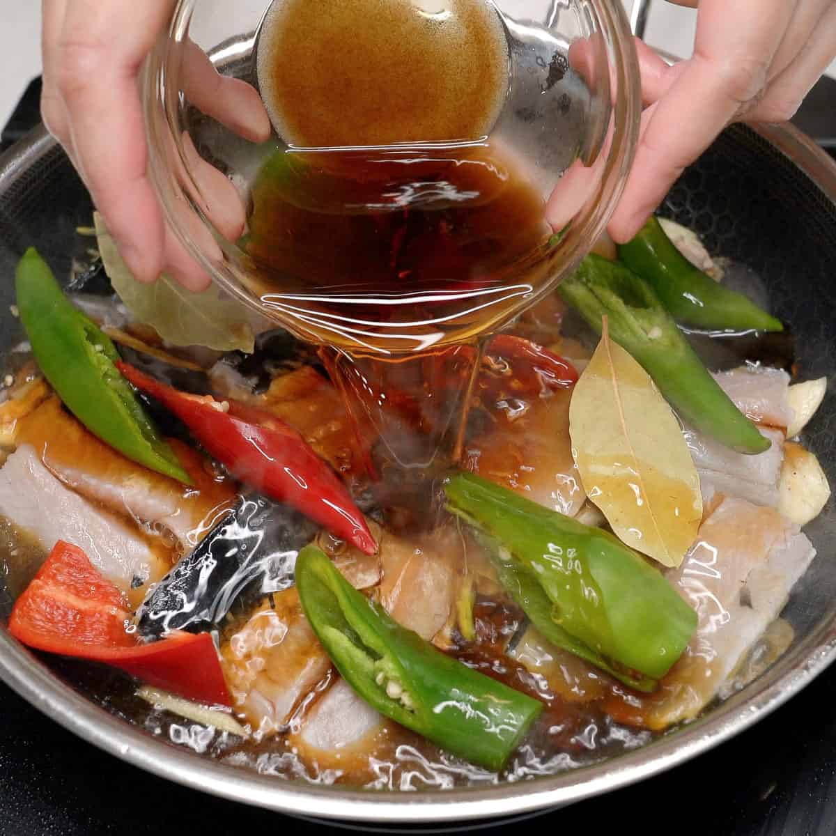 Pouring the adobo sauce over the bangus in the pan.