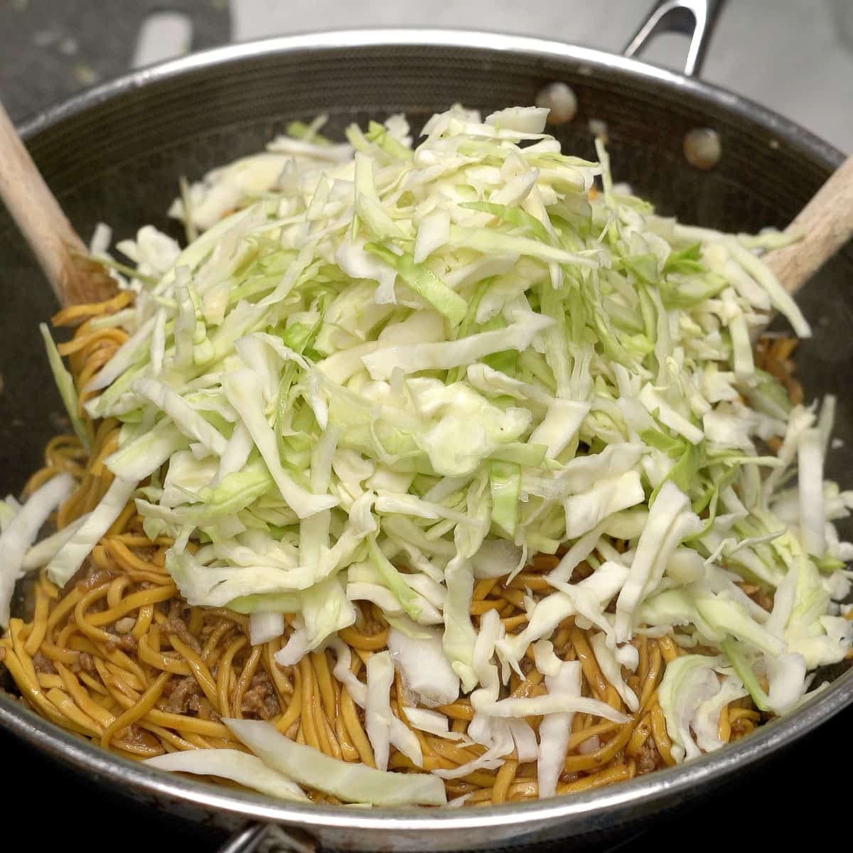 Adding cabbage to the pancit in the wok.