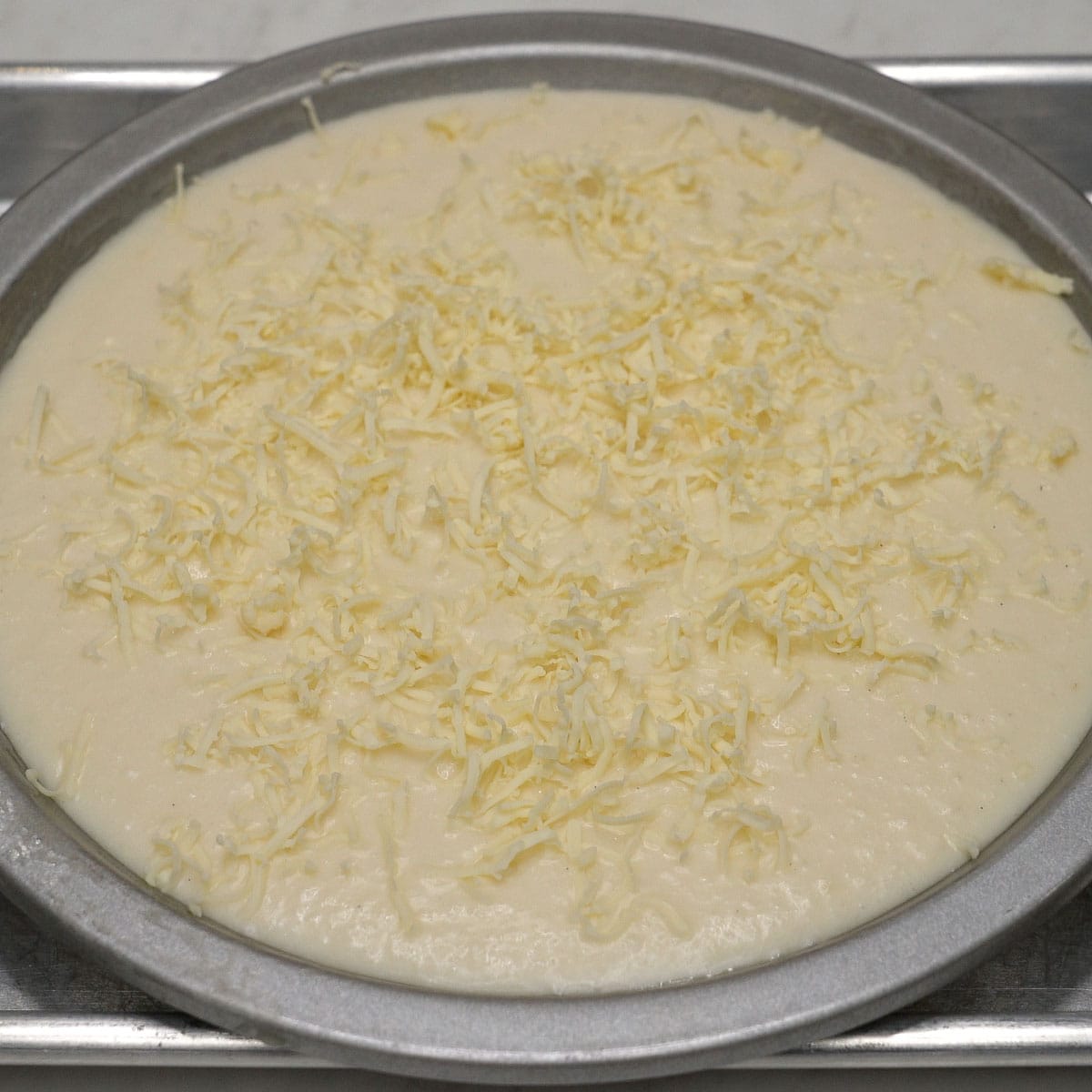 Cassava cake (budin) mixture topped with grated cheese ready to be baked.