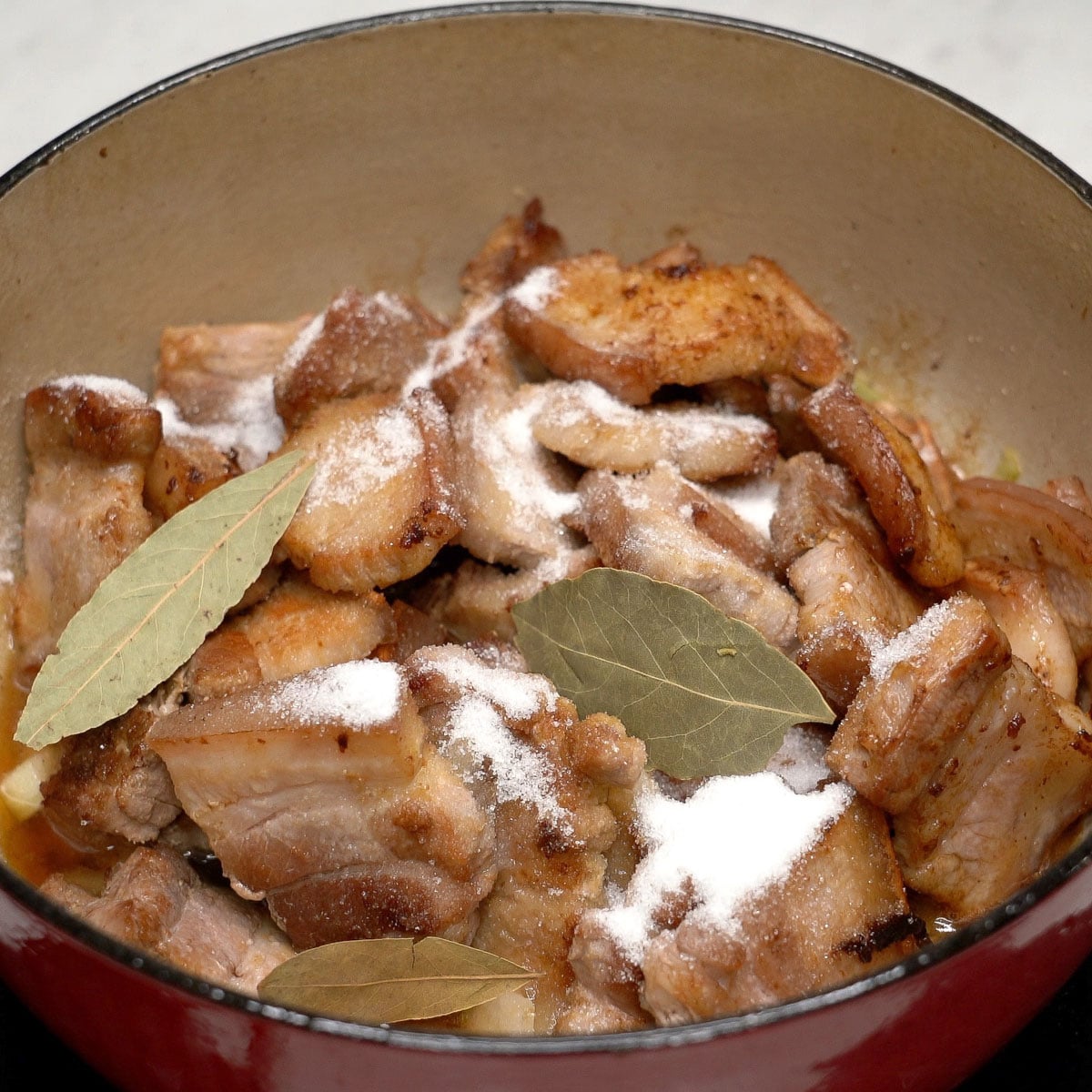 Pork with adobo ingredients in a pot.
