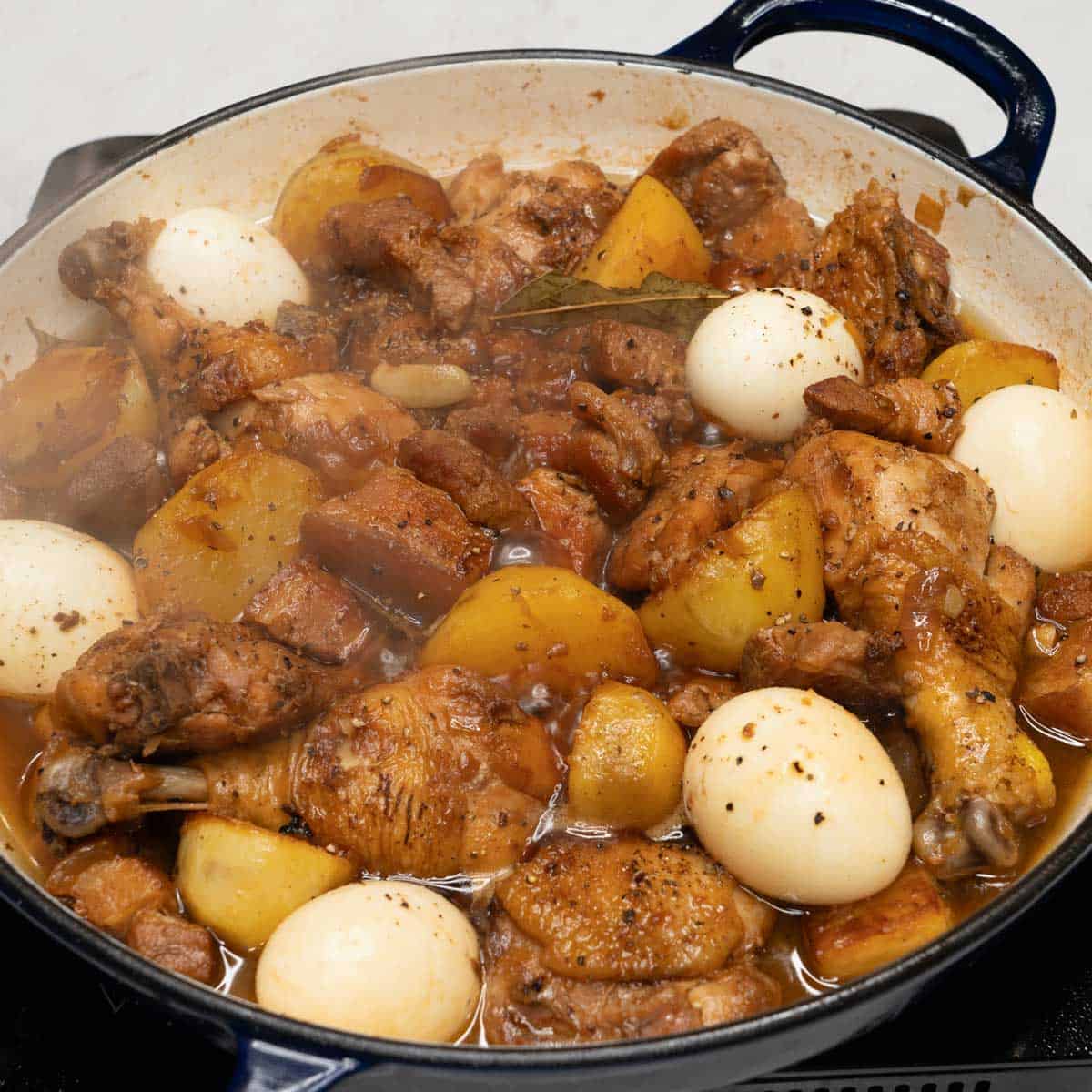 Cooked chicken and pork adobo (with potatoes and eggs) in a pan.