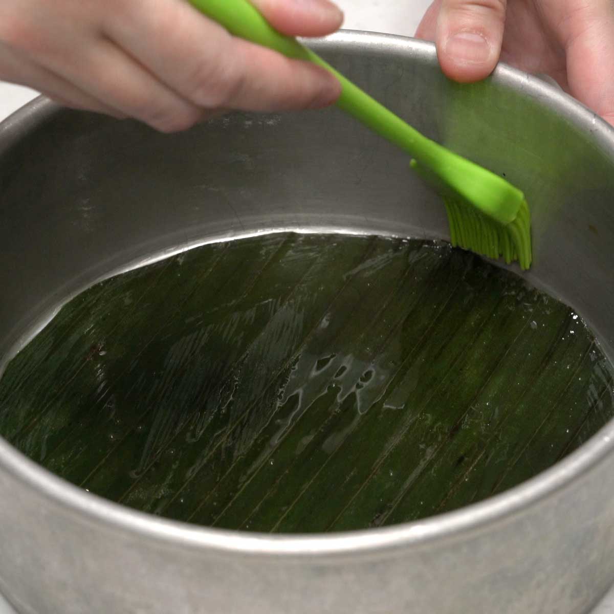 Greasing the pan lined with banana leaves.