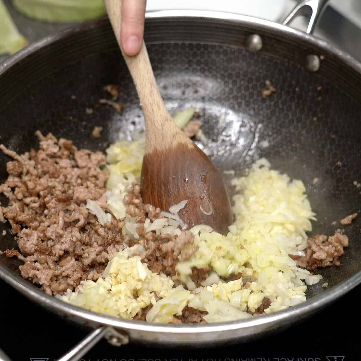 Sauteing aromatics with browned pork in a pan.