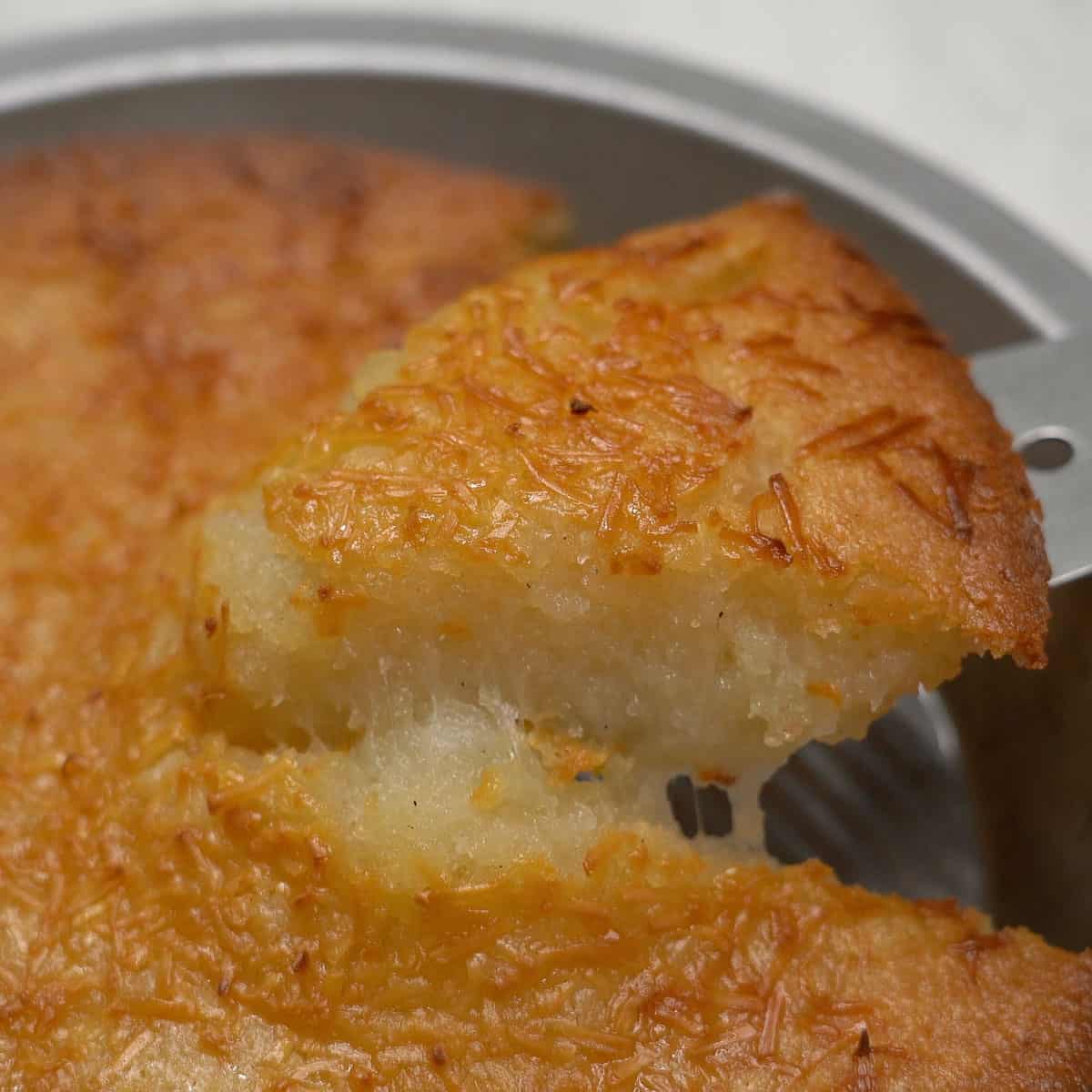 Lifting the cassava cake (budin) slice off of the pan.