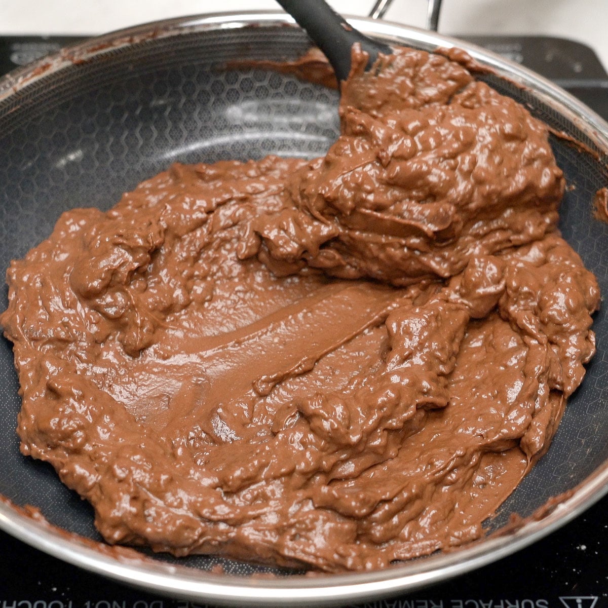 Mixing lumpy chocolate mixture using a spatula.