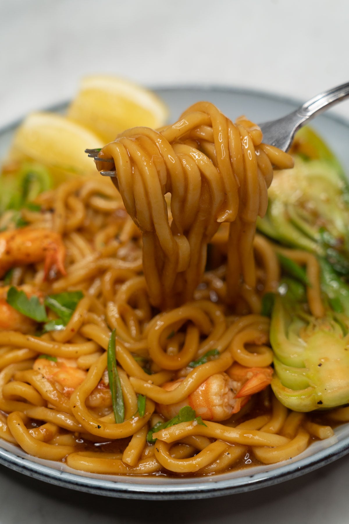 Fork lifting saucy pancit chami with shrimp from a bowl.