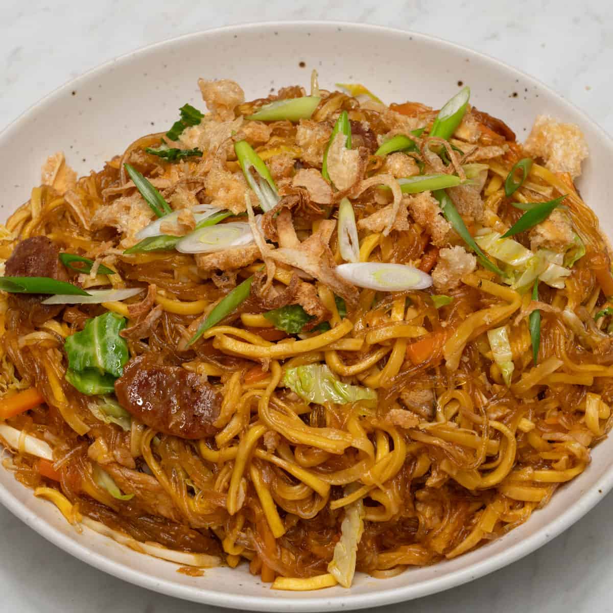 Pancit bam-i with carrots and cabbage, topped with chicharon and scallions.