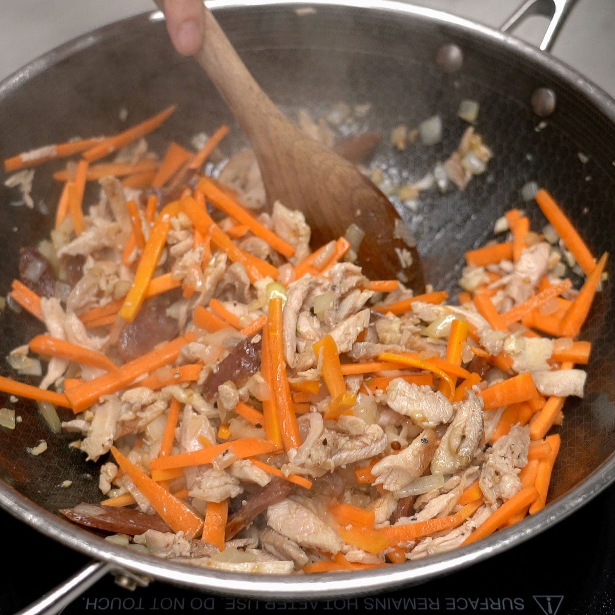 Mixing the aromatics with shredded chicken and carrots in the pan.
