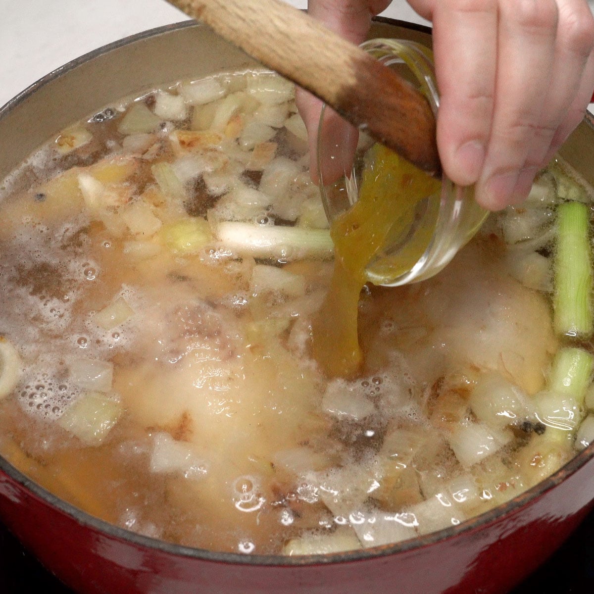 Adding chicken base to the pot of chicken and aromatics.