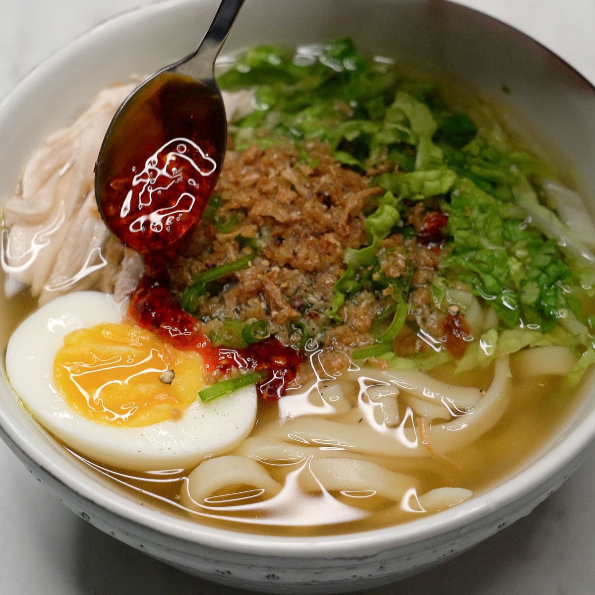 Adding chili oil to the chicken mami in the bowl.