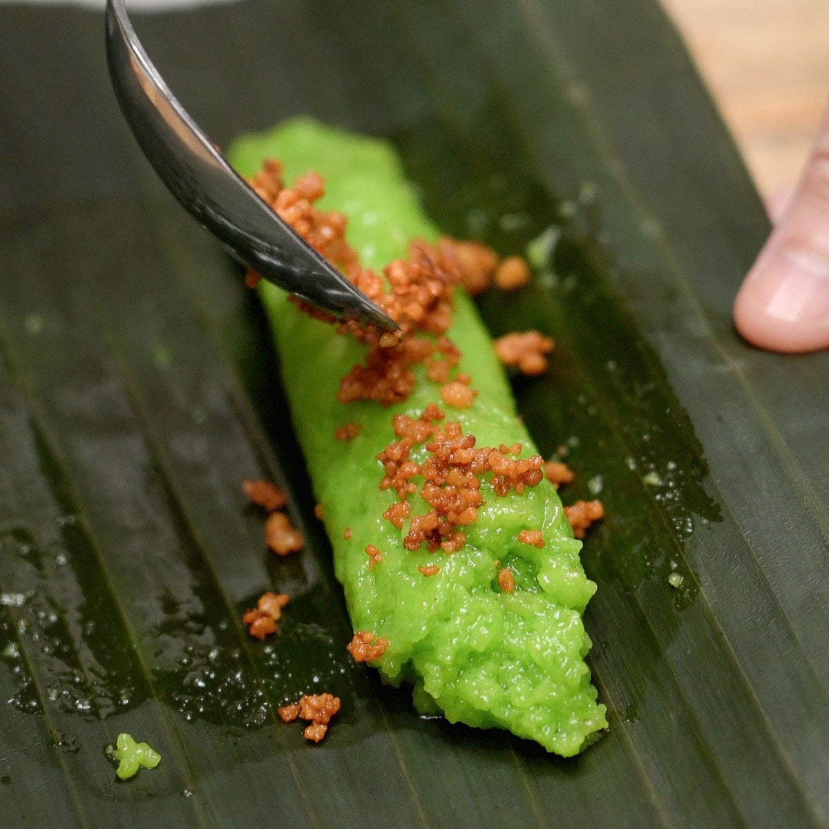 Adding latik to suman pinipig on a banana leaf.