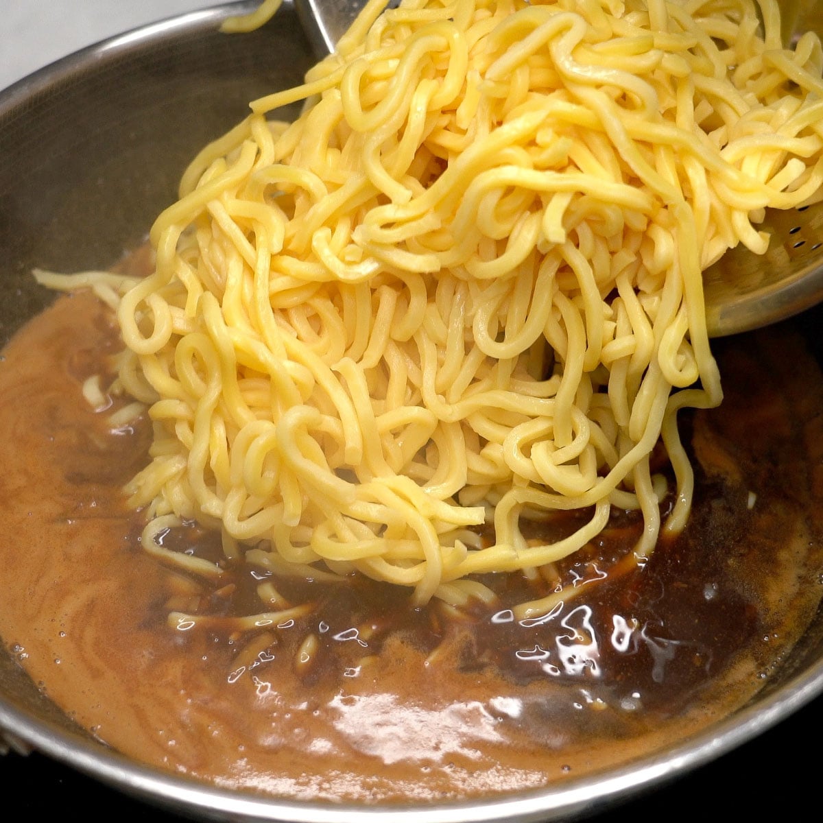 Adding fresh miki noodles to the sauce in the wok.
