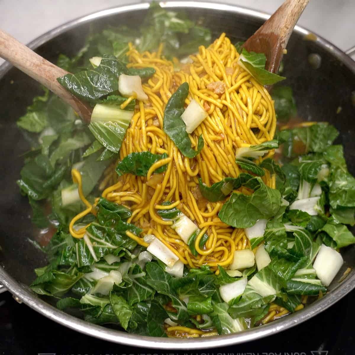 Tossing pancit bato noodles with pechay in a wok.