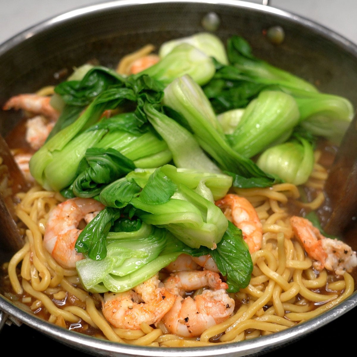 Adding shrimp and bok choy to pancit chami in the wok.