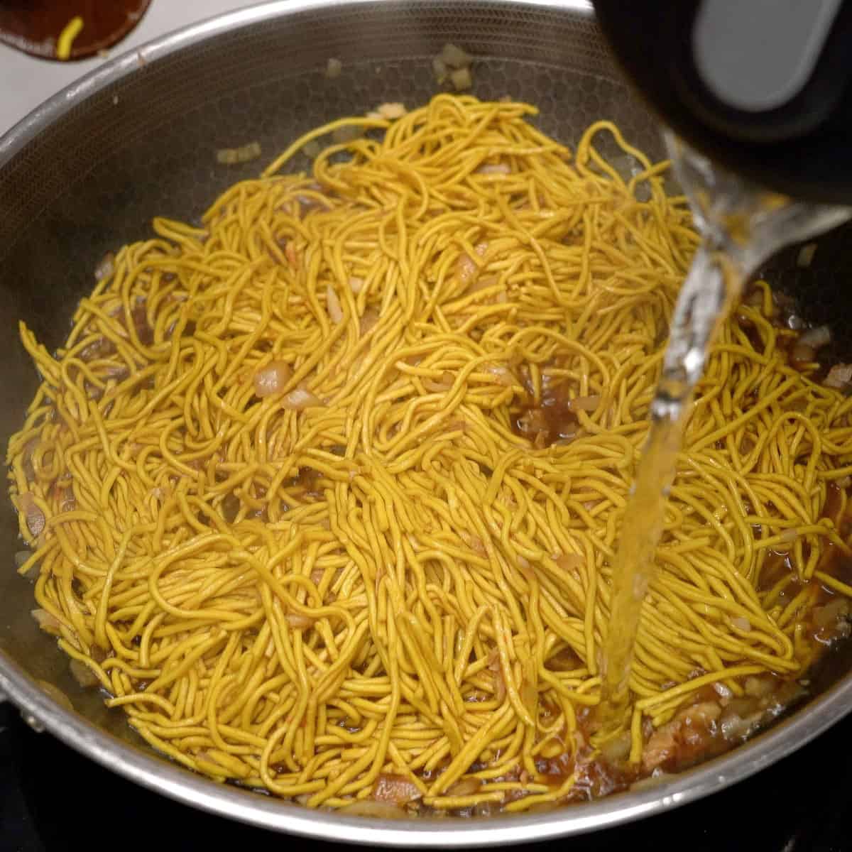 Pouring hot water over pancit bato noodles in a wok.