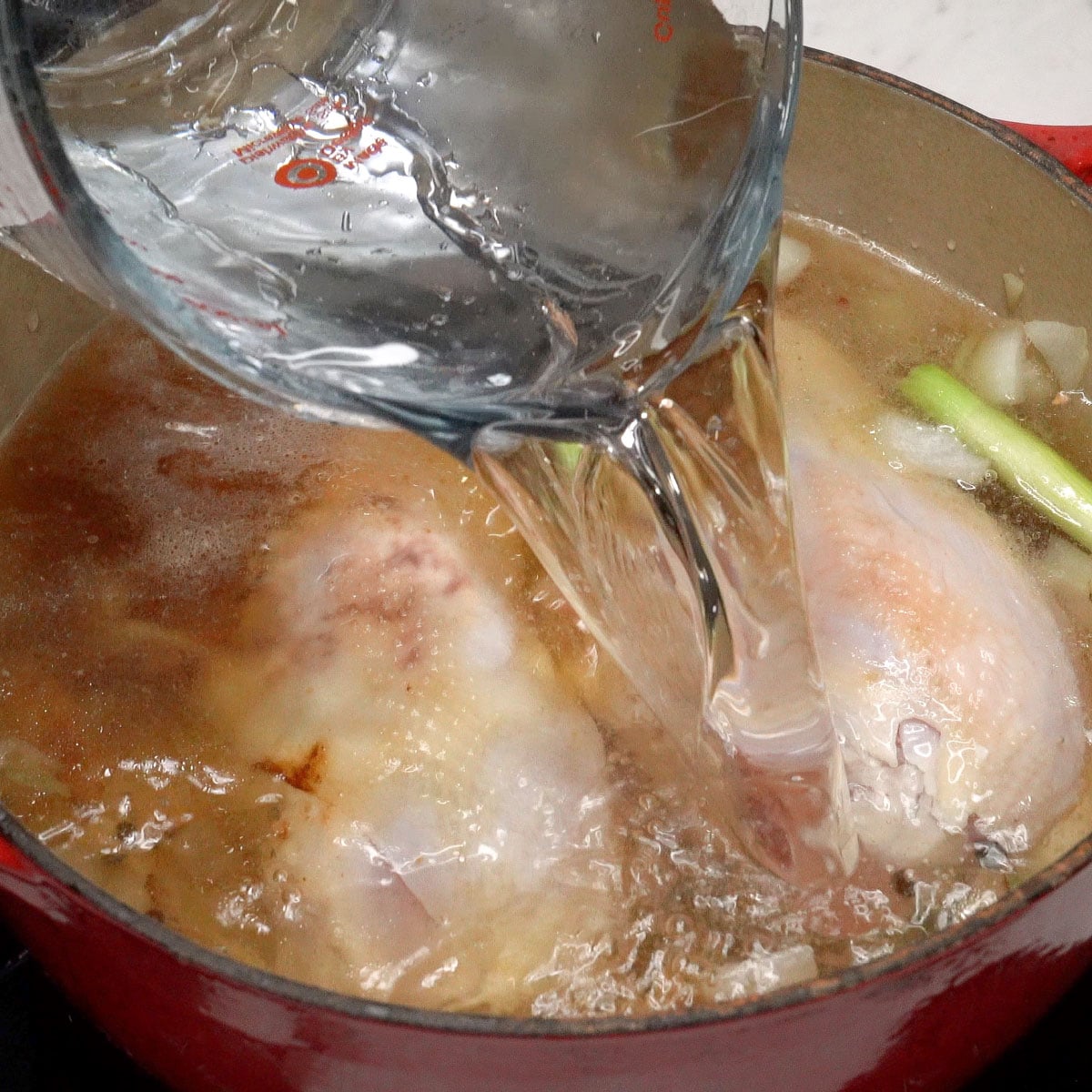 Pouring water into the pot with chicken and aromatics.