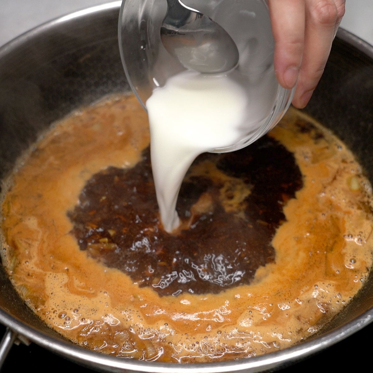 Adding cornstarch slurry to the simmering sauce in the wok.