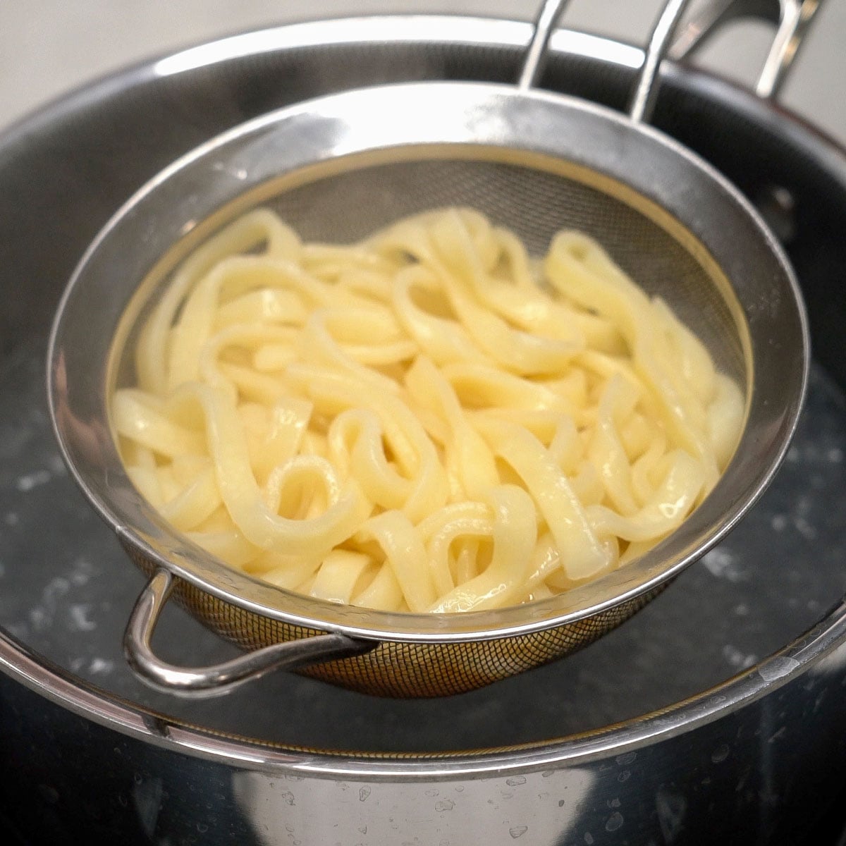 Fresh mami noodles on a strainer over boiling water.