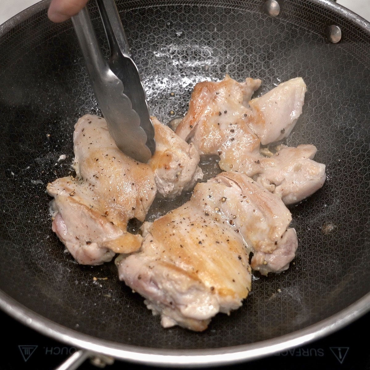 Searing chicken thighs in a wok.