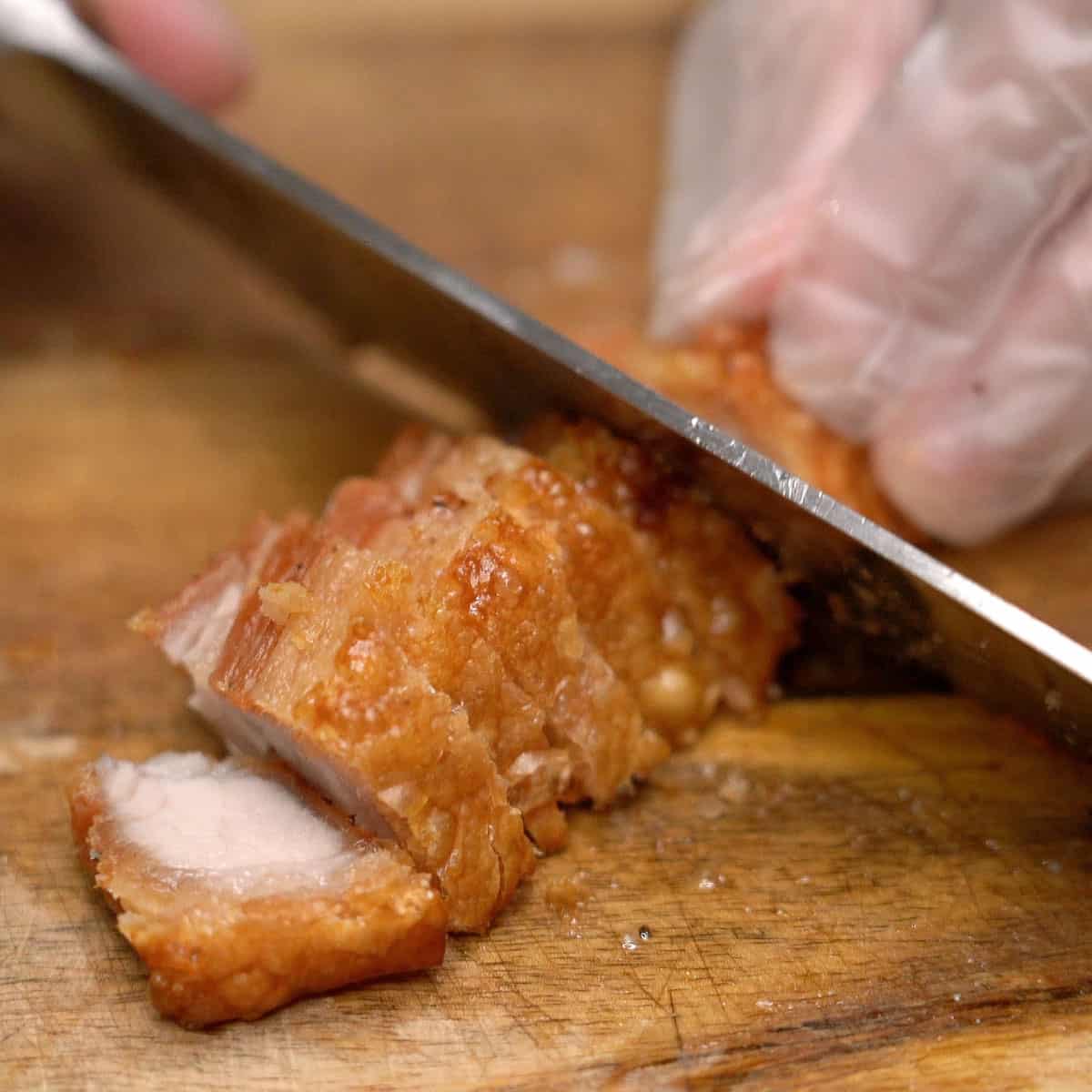 Chopping air-fried pork belly on a cutting board.