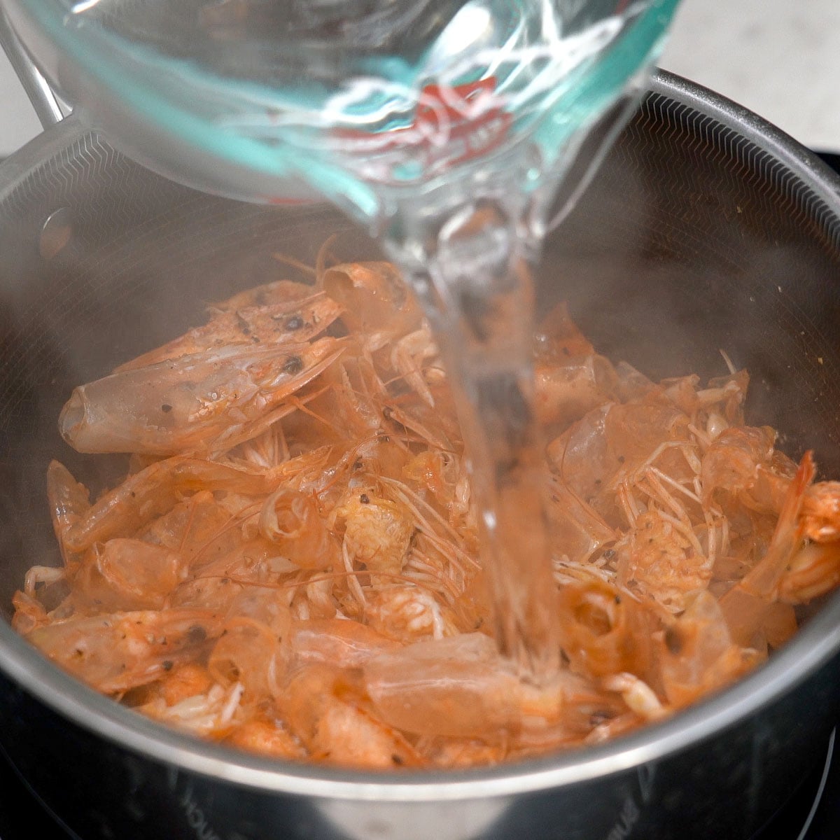 Adding water to the sauteed shrimp heads and shells in the pot.