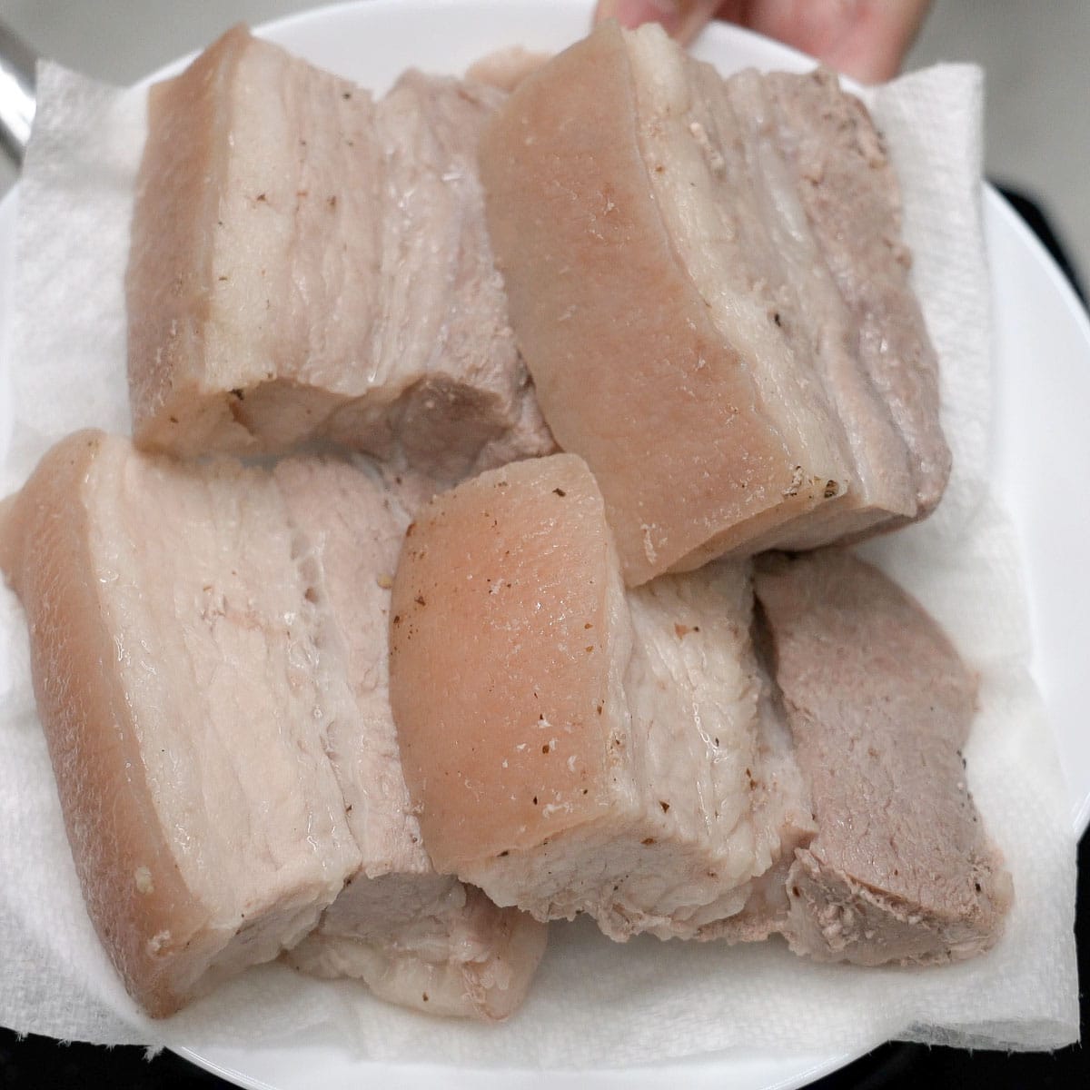 Boiled pork belly on a paper towel-lined plate.