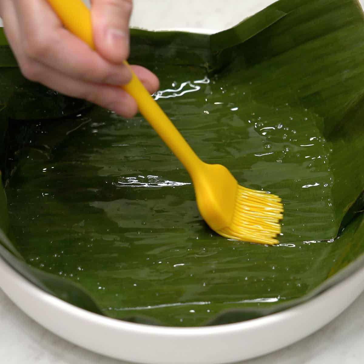 Brushing the banana leaves in the dish with coconut oil.