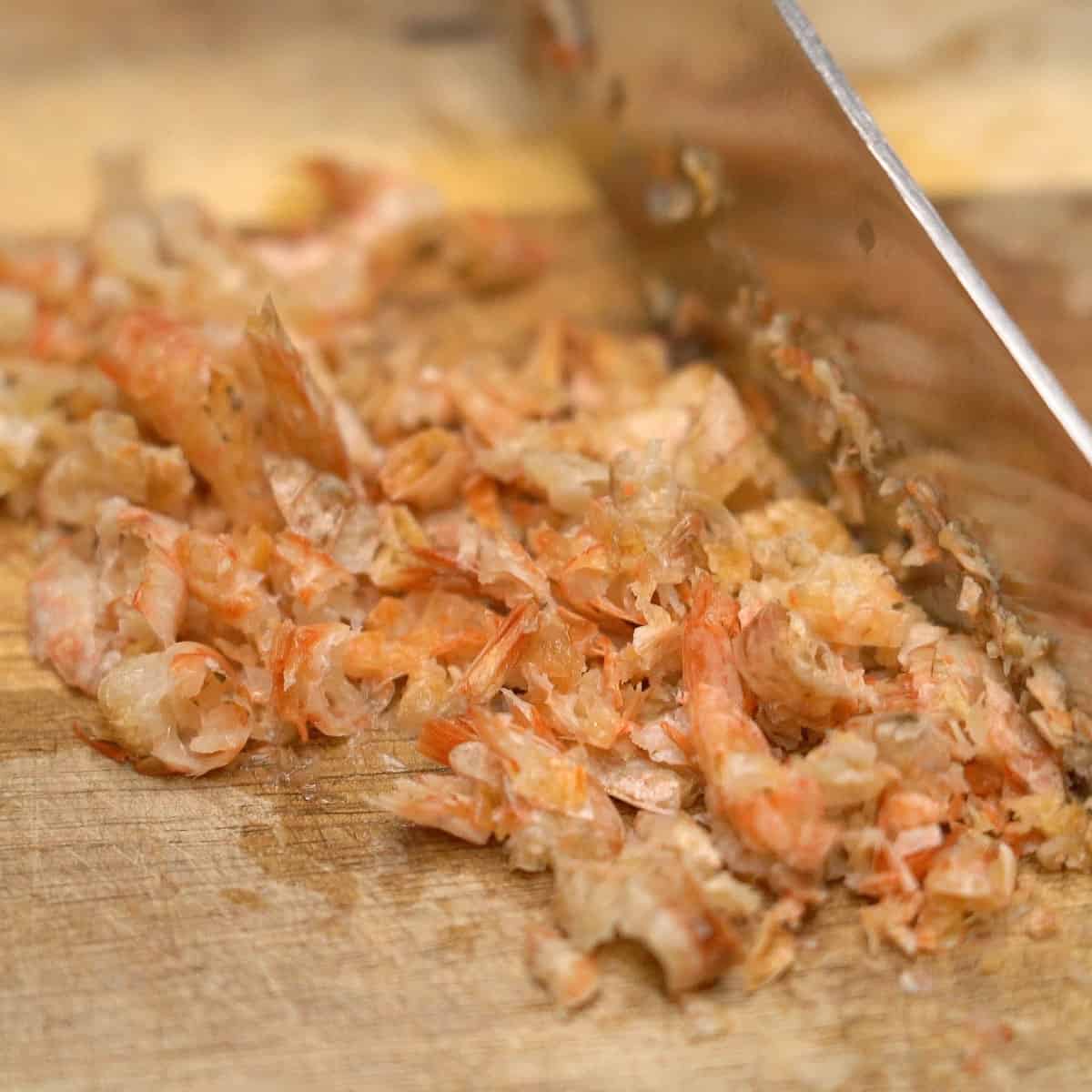 Chopping dried shrimp on a cutting board.