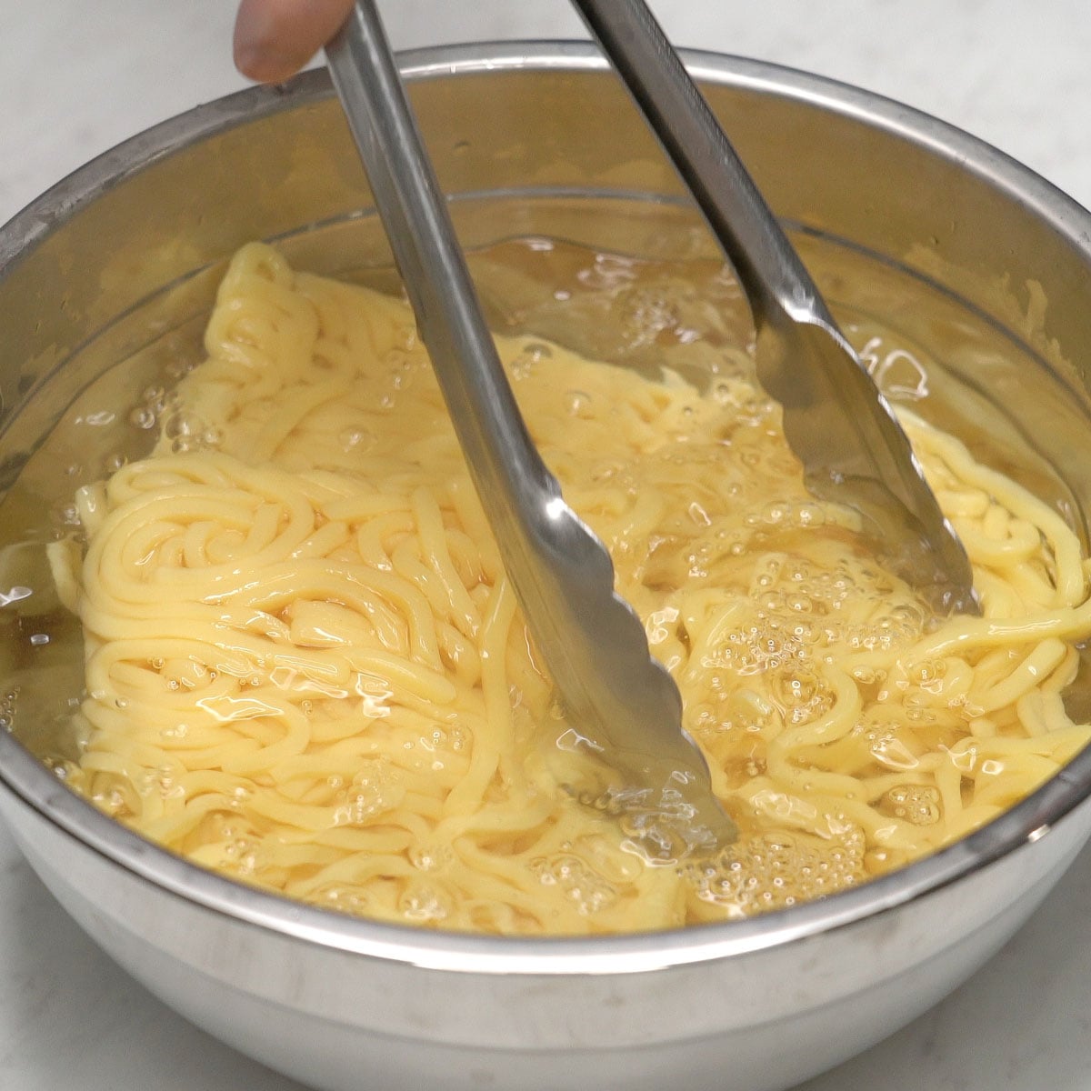 Fresh miki noodles in a bowl of hot water.