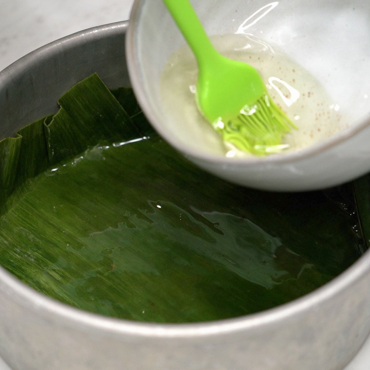Greasing the pan lined with banana leaves.