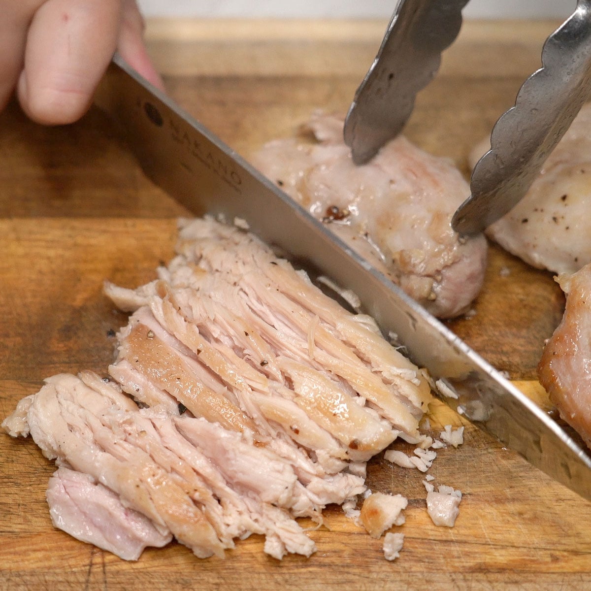 Slicing the seared chicken thighs on a cutting board.