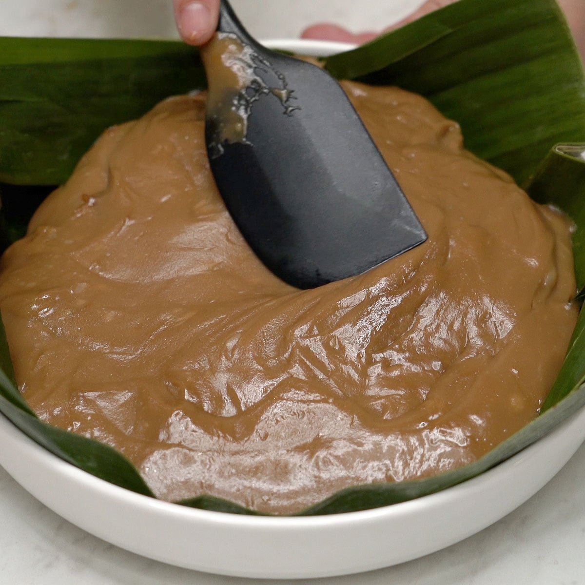 Spreading kalamay hati in a dish using a spatula.