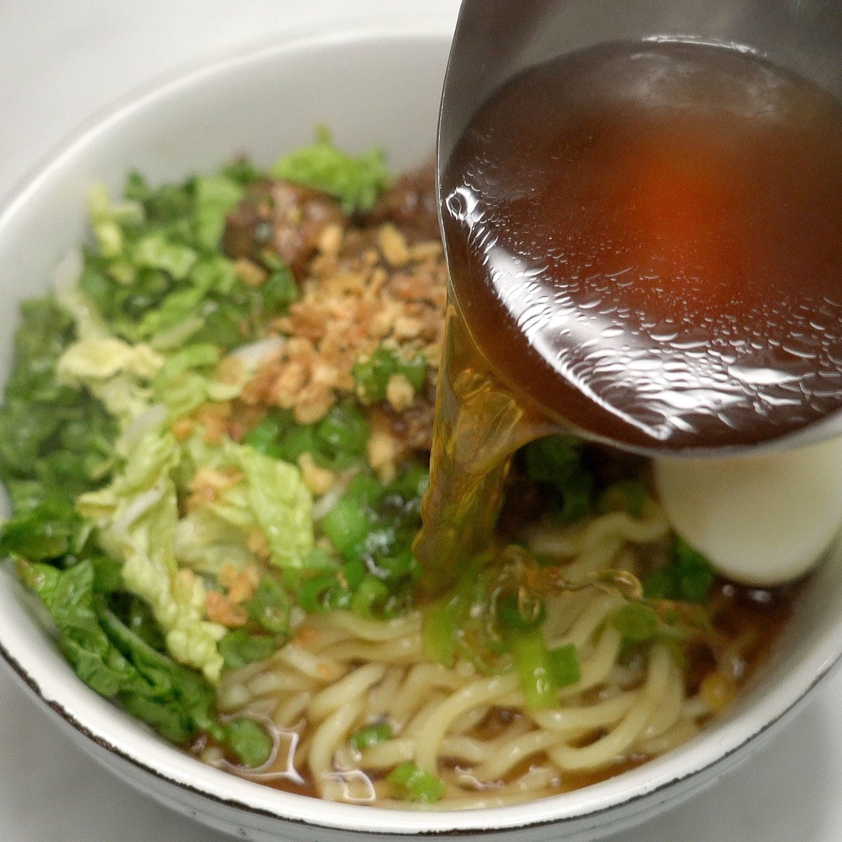Adding the broth to the assembled beef mami in a bowl.