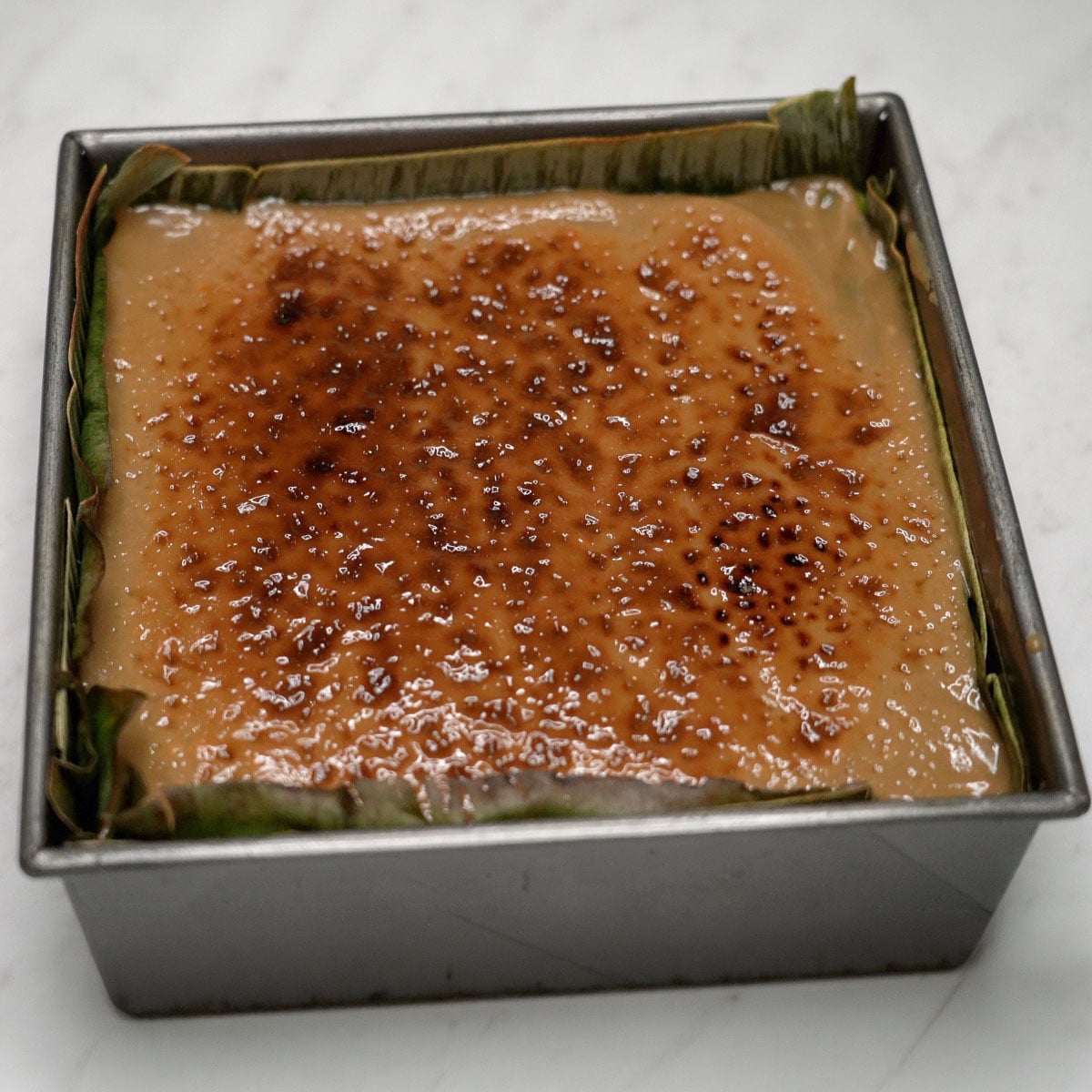 Bibingkang pinipig in a pan with broiled top.
