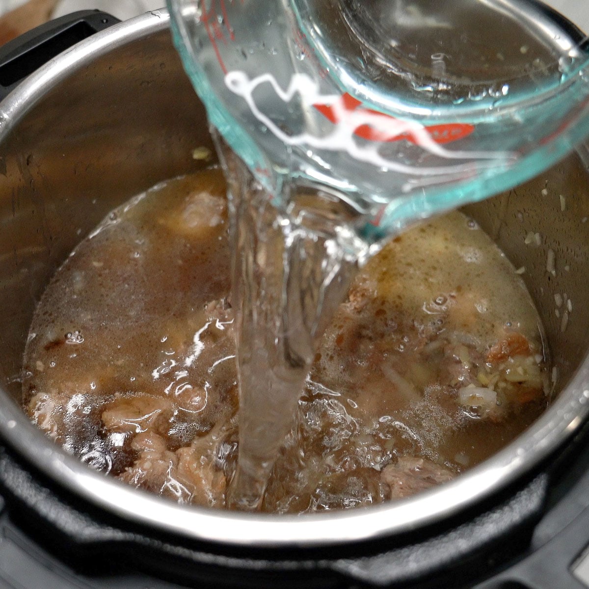 Adding water to the beef in a pot.