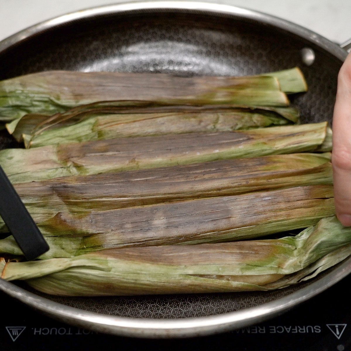 Tupig wrapped in banana leaves cooking in a pan.