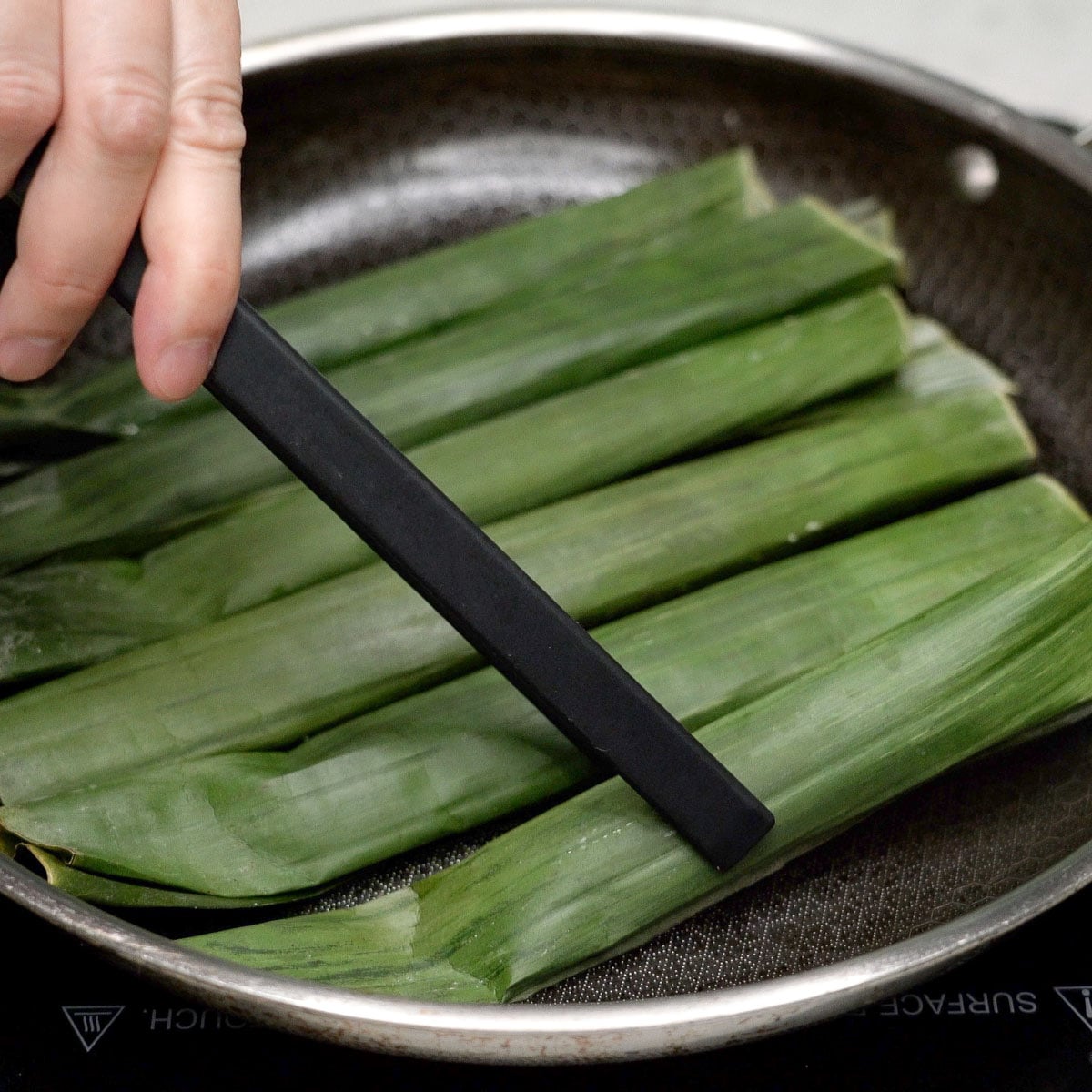 Tupig wrapped in fresh banana leaves cooking in a pan.