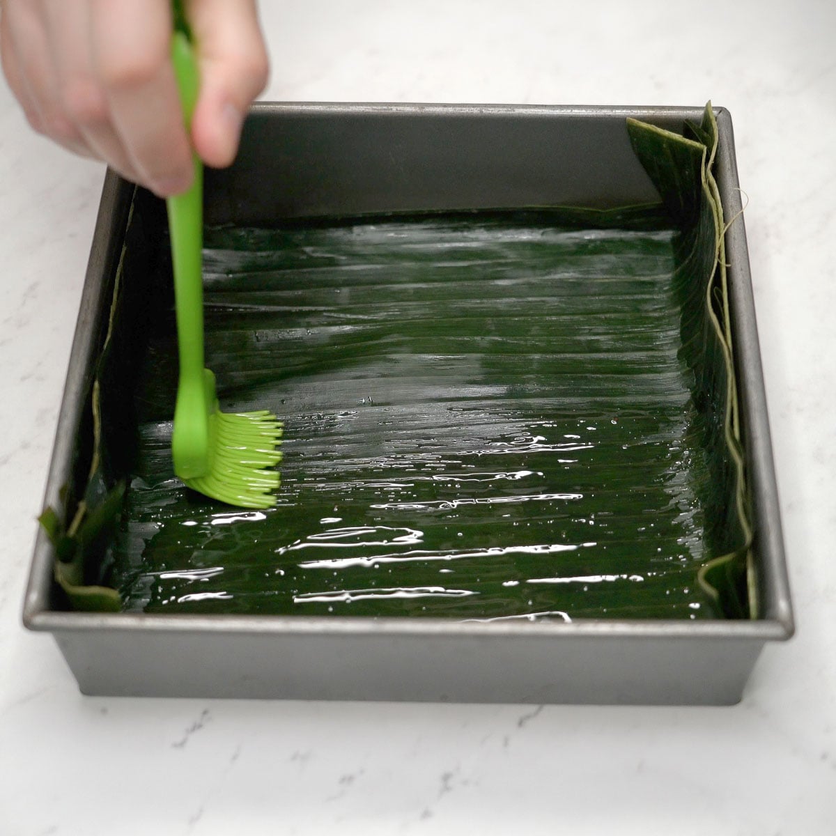 Brushing oil on banana leaves in the pan.