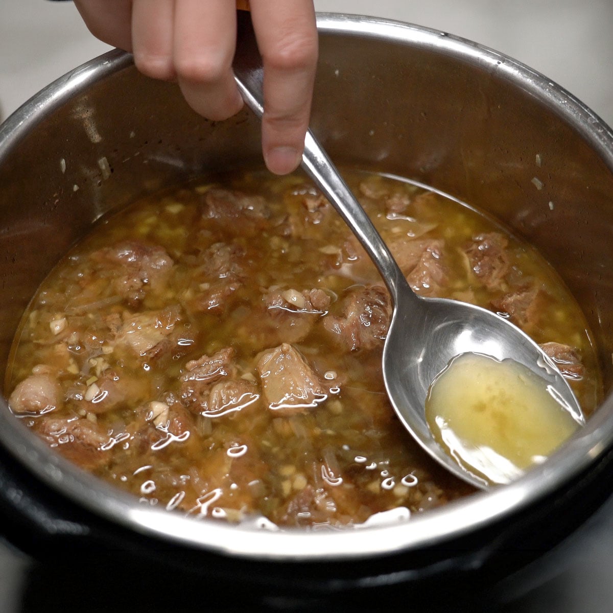 Removing the oil on top of the beef in the pot.