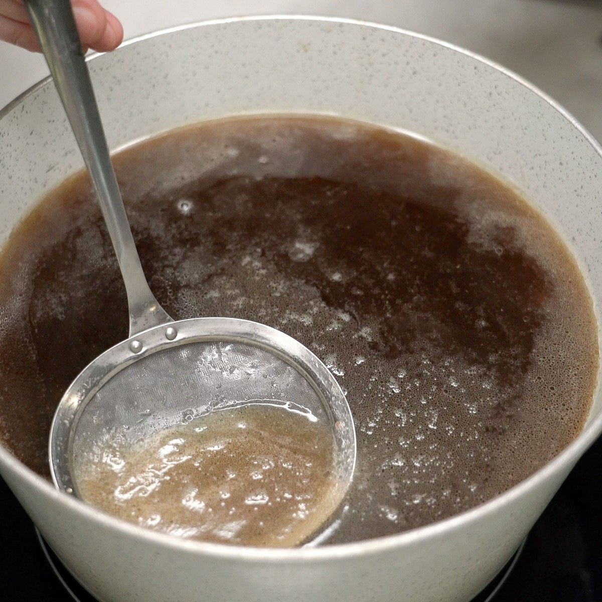 Skimming the fat on top of the broth in a pot.