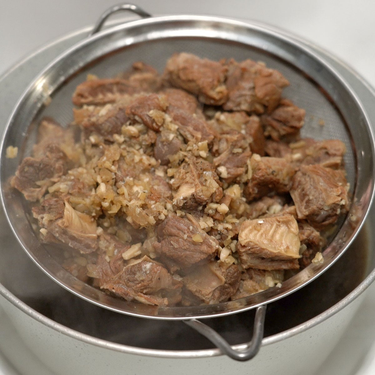 Straining the beef over a pot of broth.