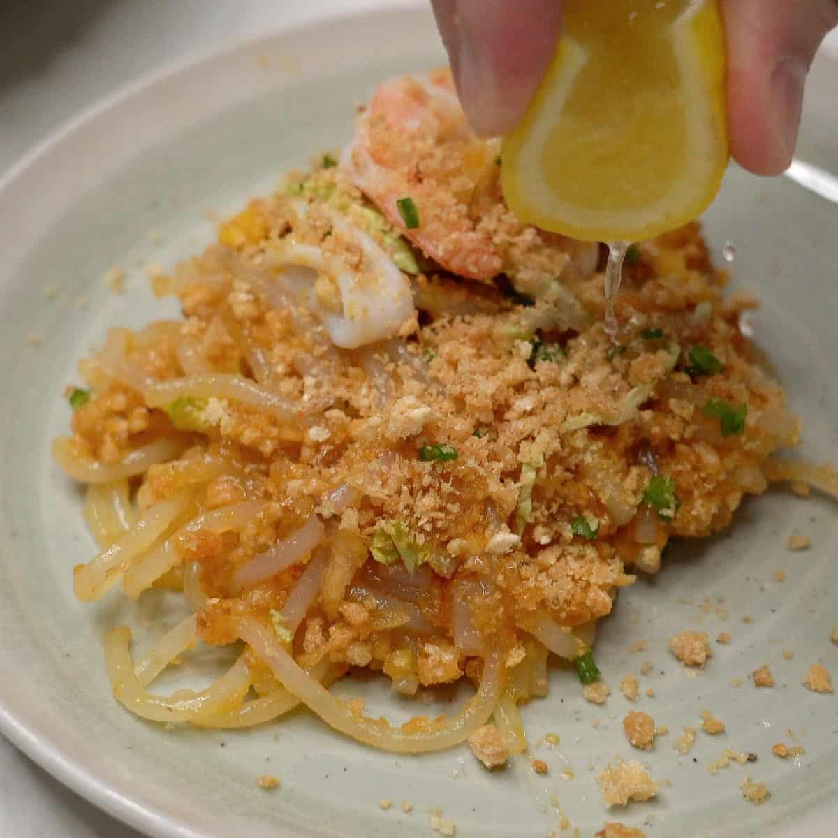 Squeezing lemon over pancit malabon on a plate.