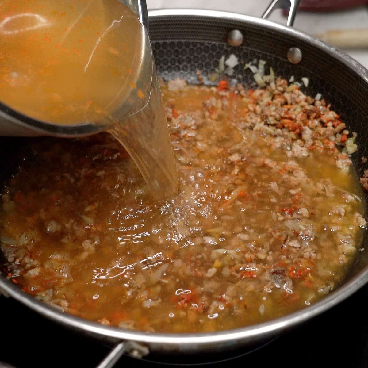 Adding the shrimp stock to the mixture in the wok.