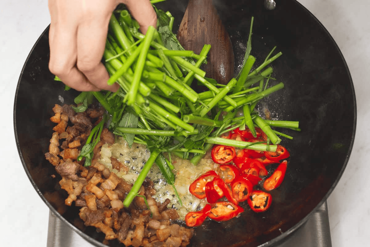 Adding the kangkong stems into the wok.