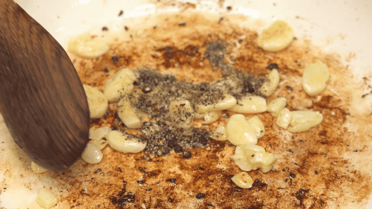 Sauteing garlic and crushed peppercorns in a saute pan.