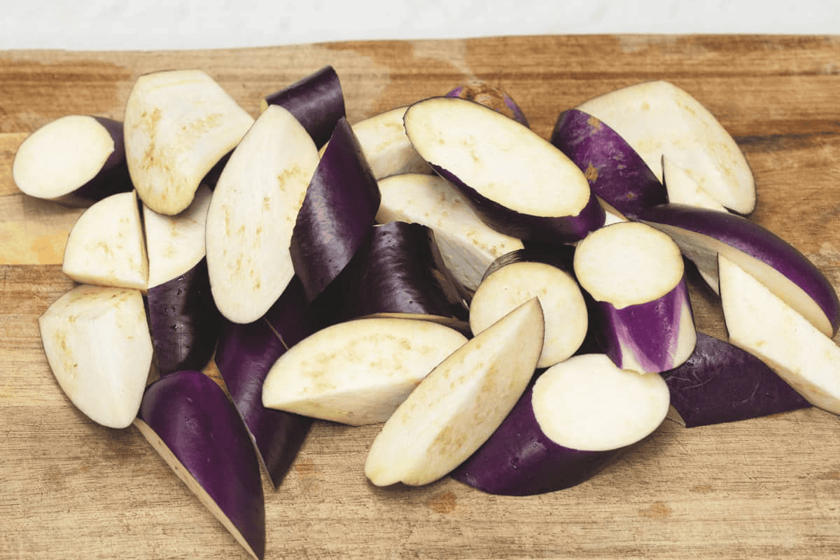 Eggplant cut into diagonal pieces on a cutting board.