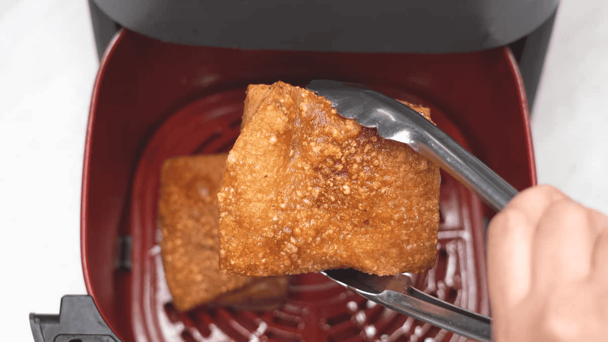 Holding the air fried pork belly with a pair of tongs over the air fryer basket.