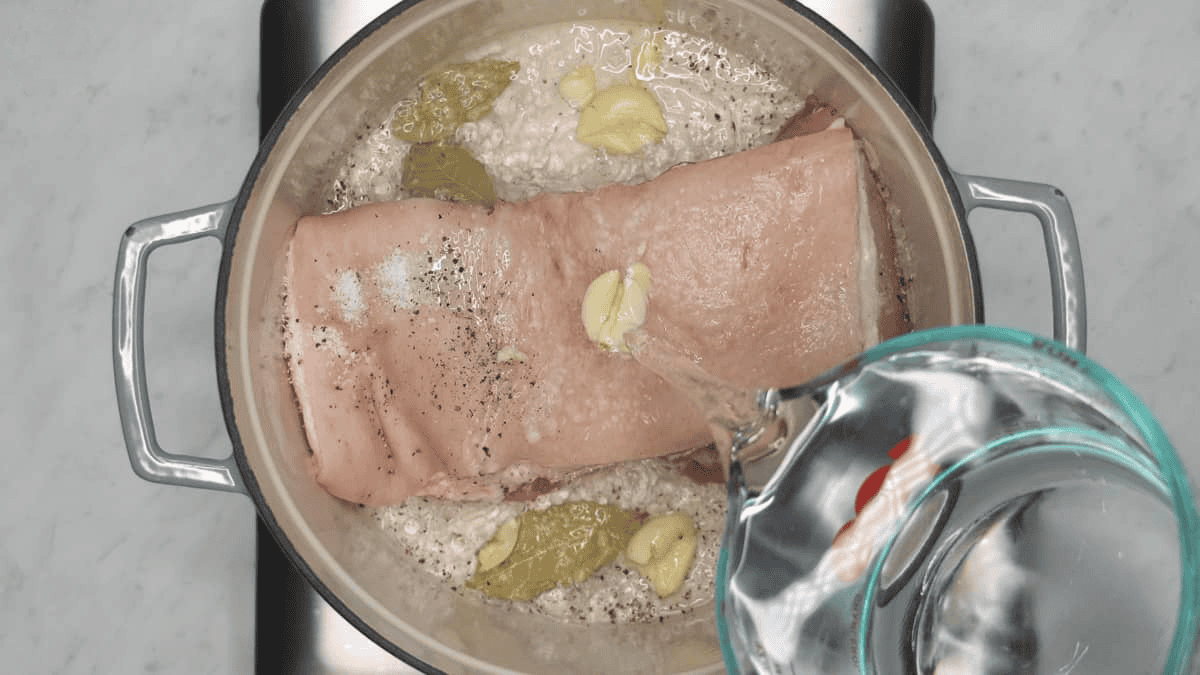 Adding water to pork belly and other ingredients in the Dutch oven.